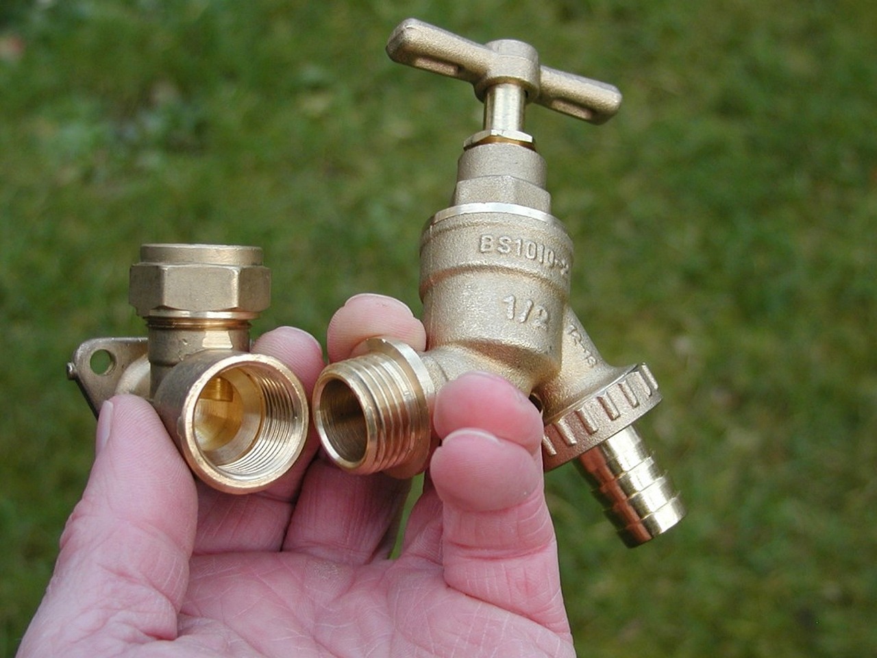 Hand holding brass plumbing fittings — a bib tap and a wall plate elbow