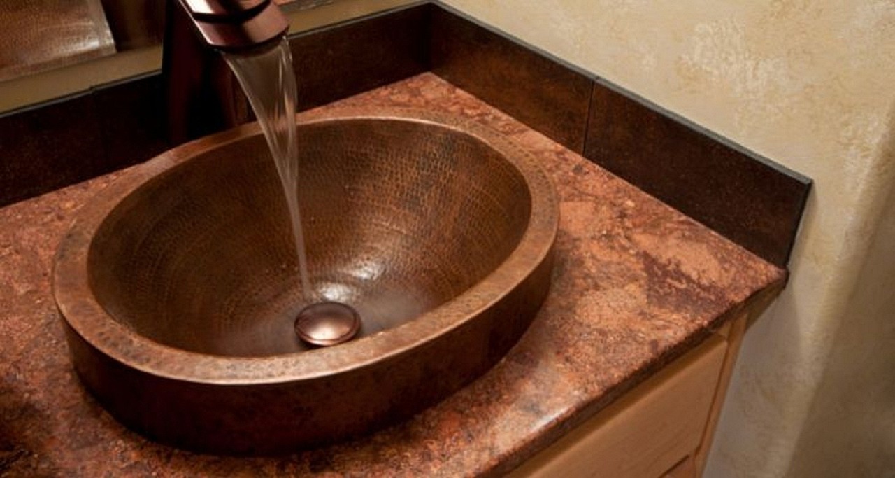 Water running from a dark tap into a hammered copper basin on a stone benchtop