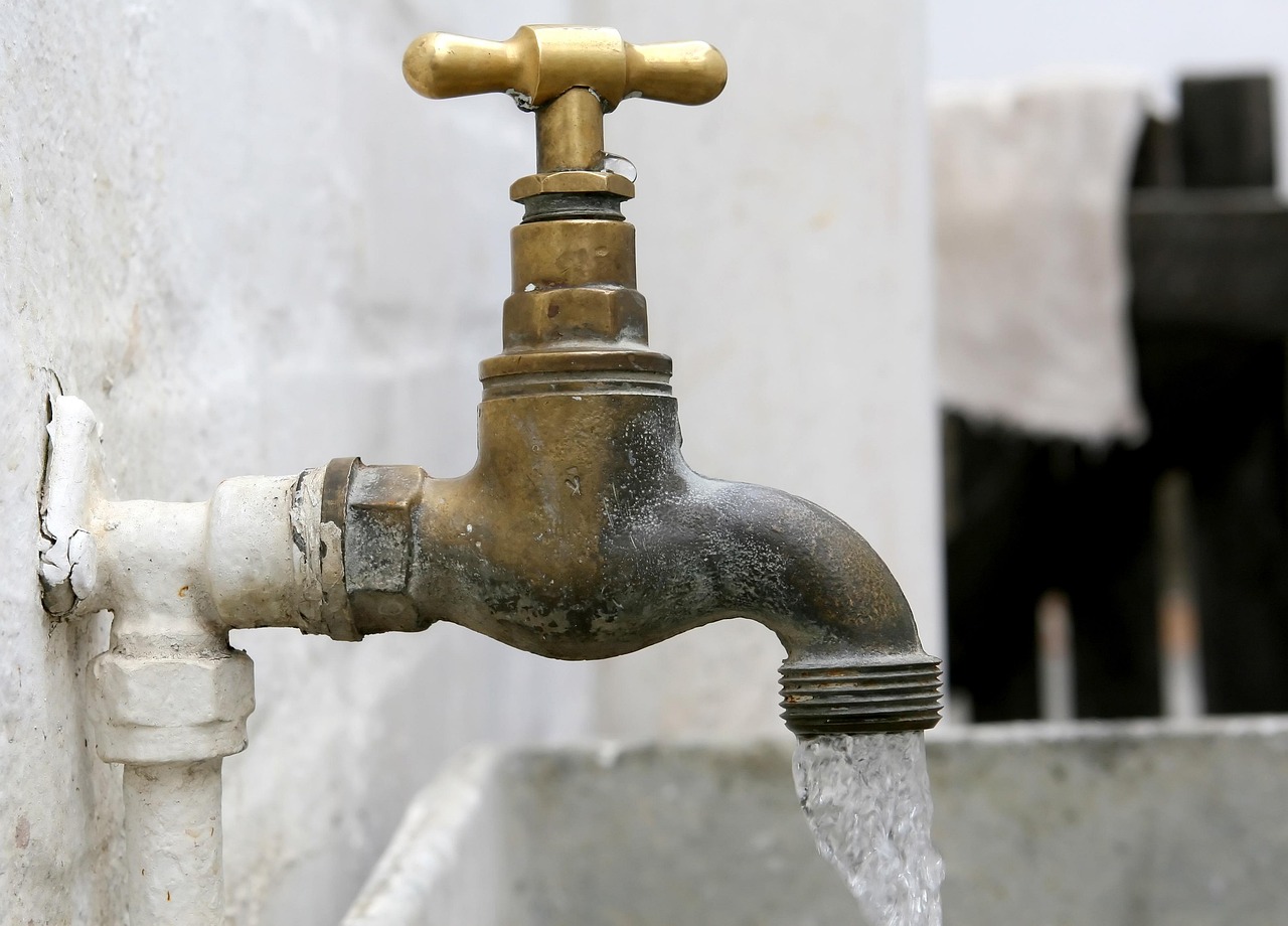 Water running from an old brass garden tap on a white laundry wall
